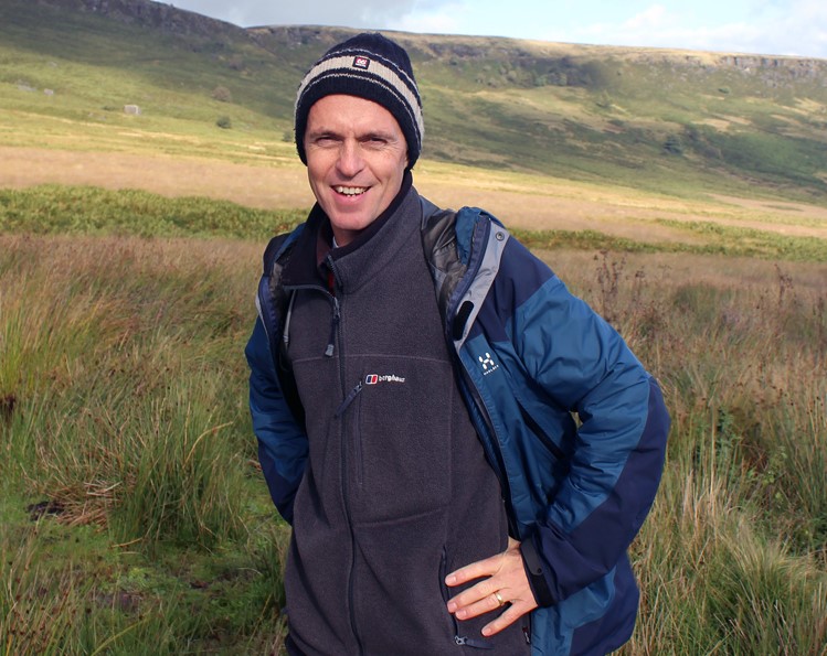 Andrew McCloy poses in outdoor clothing with a Peak District landscape behind him