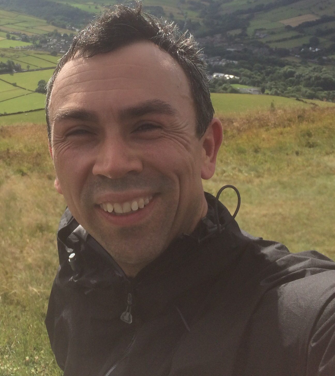 Alex Waddington smiles to the camera with a Peak District landscape in the background