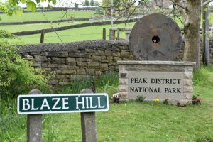 The circular millstone on a plinth with a road sign in the foreground reading Blaze Hill
