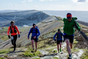 Four fell runners with a Peak District landscape in the background