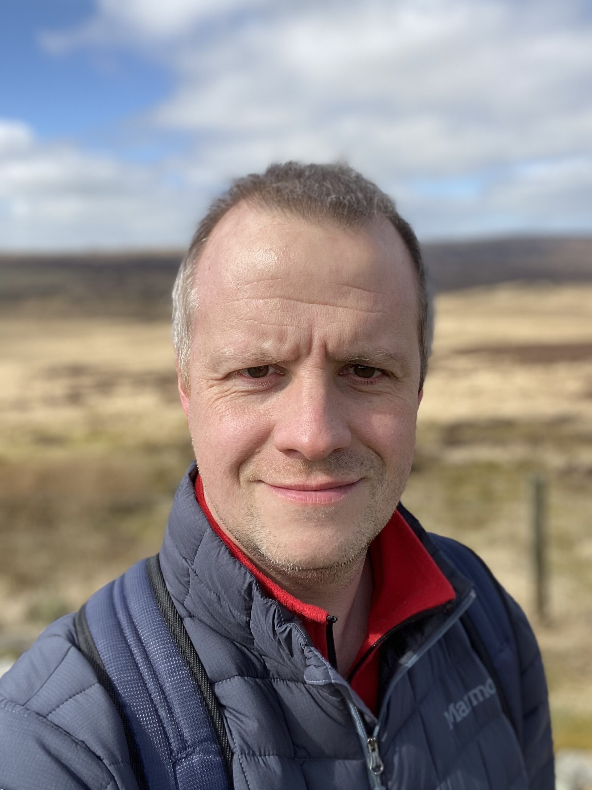 A man wearing a coat smiles in front of blue sky in the Goyt Valley.