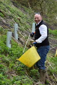 A member of the Bumper team smiles at the camera while holding a litter picker and yellow bucket