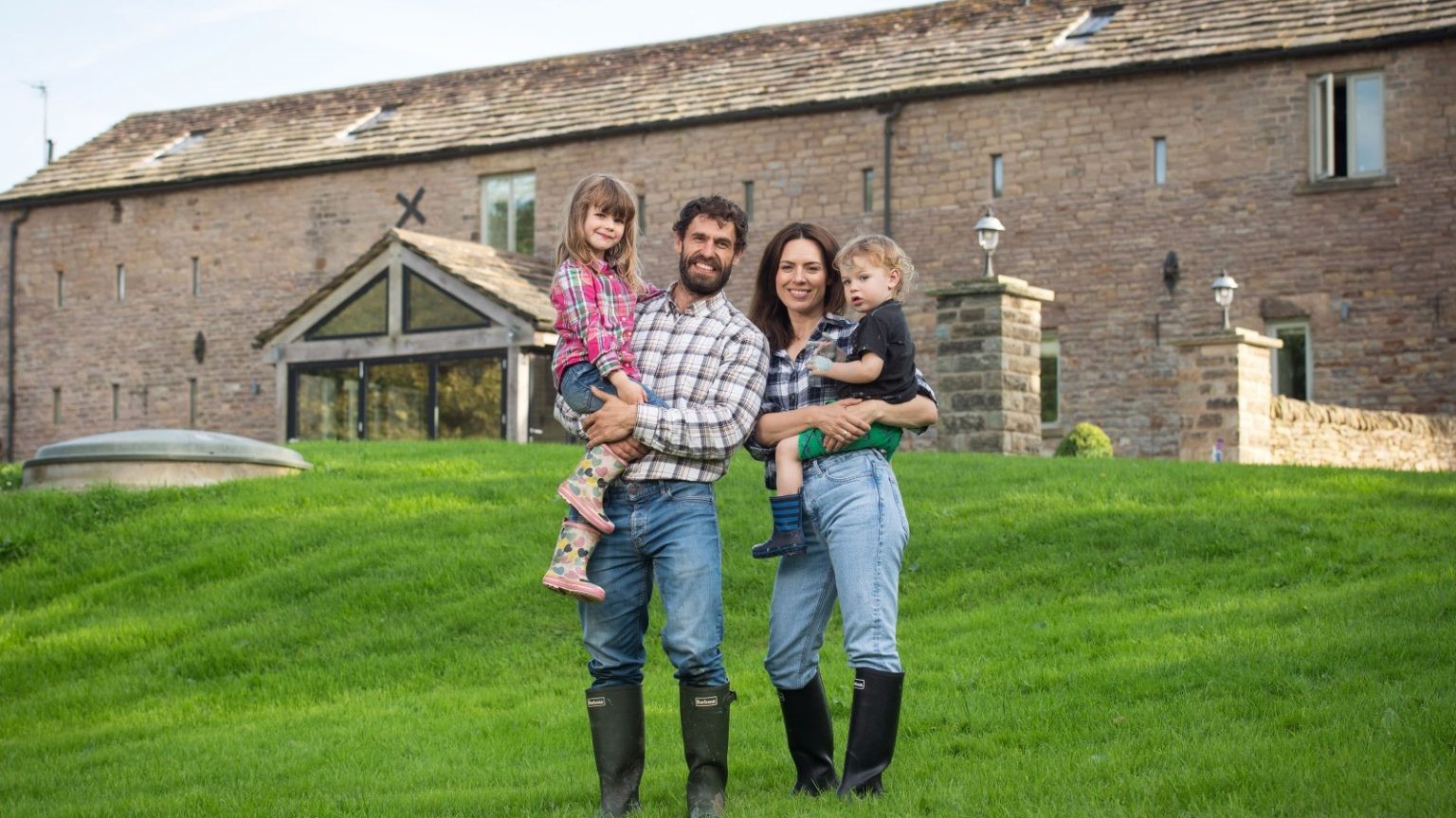 Kelvin Fletcher and his family smile at the camera with a farmhouse in the background