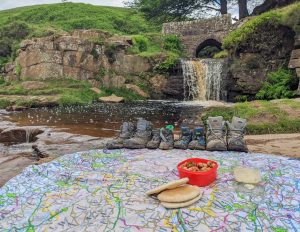 a PACMAT picnic blanket in front of a beautiful waterfall, credit Peak District Kids