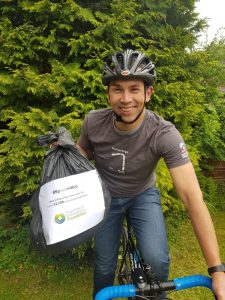 Alex Waddington on a bike holding up a bag of litter collected on the longest day around the Peak District