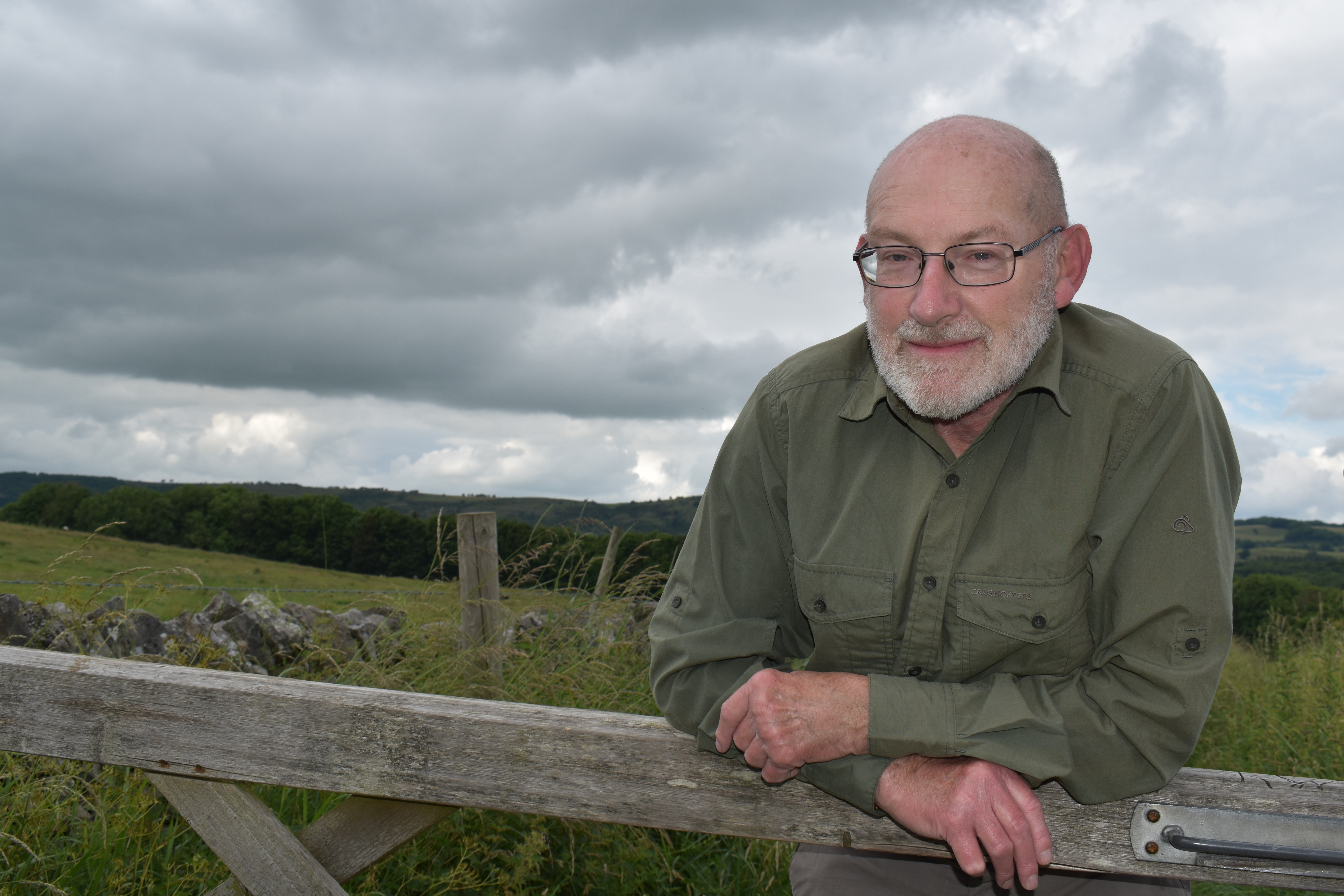 Stuart Pomeroy leans on a wooden five bar gate with a view of the moors in the background
