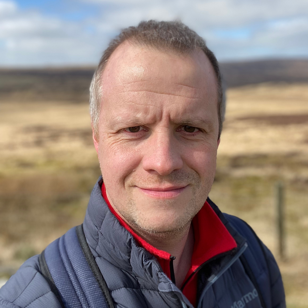 A man wearing a coat smiles in front of blue sky in the Goyt Valley.