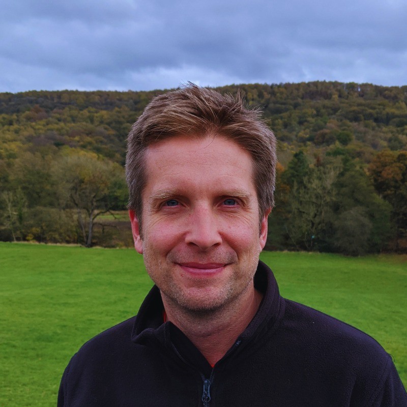 Headshot of Ben standing in a green field wearing a black fleece.