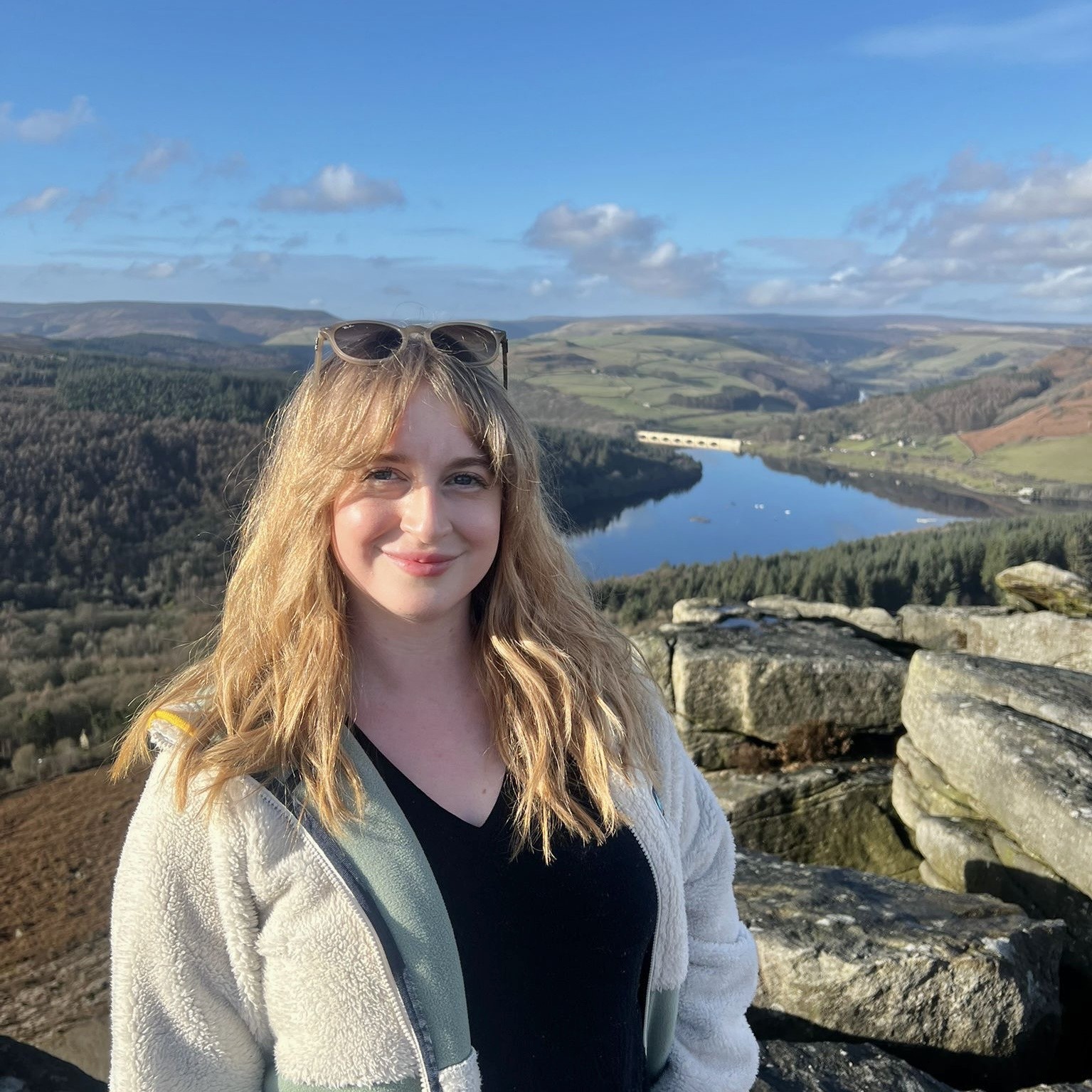 A blonde woman in a fleece stands on the rocks at Bamford Edge, overlooking water