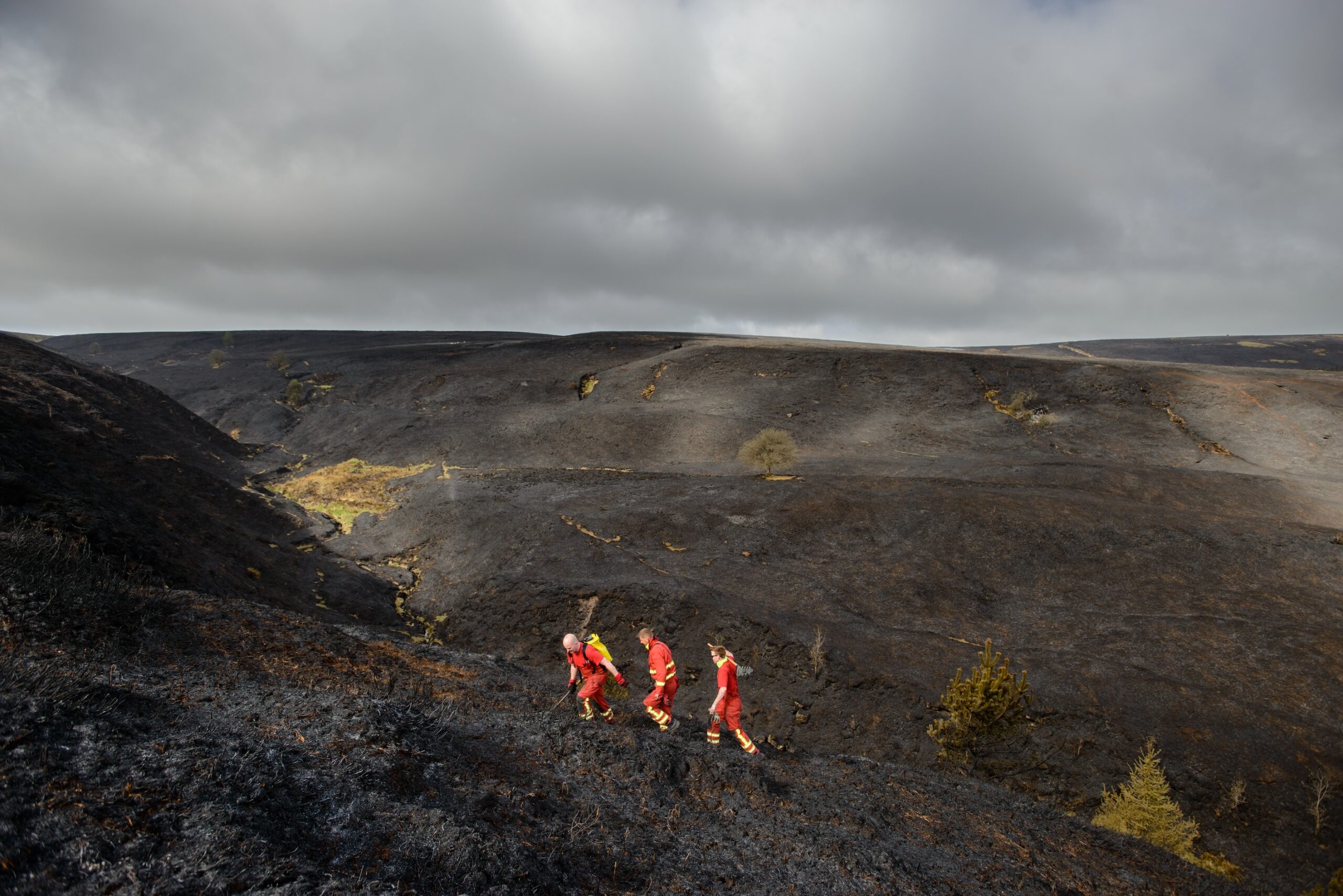 Three firefighters cross the burnt landscape of the Goyt Valley.